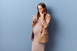 Shocked young adult pregnant woman wearing dress and jacket scrolling online looking at cell phone screen with astonished face browsing posing isolated over blue background