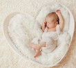 Newborn sleeping on White Fur Blanket. Baby lying in Crib. Infant Child sleep on Heart shaped Pillow