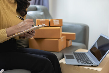 Wall Mural - Small business startup, SME owner, female entrepreneur working on receipt boxes and checking online orders, laptop to prepare to pack boxes to sell to customers. Close-up photo