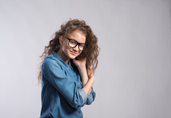 Wall Mural - Portrait of a gorgeous teenage girl with curly hair and eyeglasses. Studio shot, white background with copy space