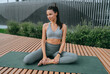 Fit young woman in athletic wear sits on a yoga mat outdoors, stretching while enjoying a tranquil urban park setting