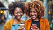 © AdriFerrer - Two women with curly hair are smiling and holding up their cell phones