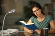Happy woman wearing eyeglass reading a paper book in the night
