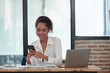© crizzystudio - African businesswoman uses smartphone while working on laptop at office African American businesswoman smiling and talking Contact and work with customers happily. Successful online business ideas.