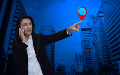 Wall Mural - Businesswoman talking on her cell phone and pointing finger to map pin point location button over modern office city tower and skyscraper, Map pointer navigation concept