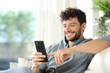 Happy man using cell phone on a couch at home