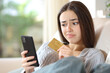Disappointed woman buying online on a couch at home