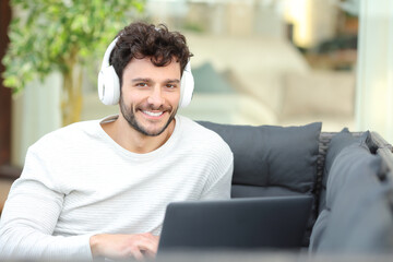 Happy man with headphone and laptop looks at you at home