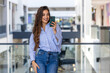 Happy confident young business woman using cell mobile phone . Smiling lady professional holding cellphone standing in the modern building looking away working outside office.