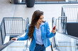Smiling young business woman wearing suit standing on urban escalator using applications on cell phone, reading news on smartphone, fast connection, checking mobile apps outdoors.
