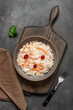 Sauerkraut with cranberries and carrots in a bowl on a wooden cutting board, dark rustic background. Top view, flat lay, vertical.