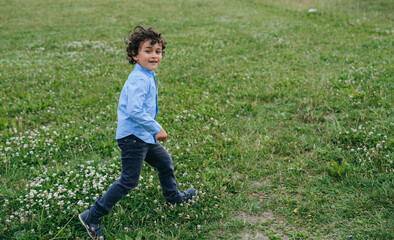 Playful young boy with curly hair running joyfully across a blooming meadow, embodying the freedom and excitement of childhood