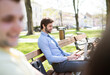 Handsome businessman sitting on city bench, typing on laptop. Working remotely from city park, waiting for business meeting. Manager smiling, outdoor in urban setting
