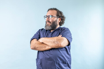 plump serious male doctor with beard on blue background and blue sanitary uniform, looking left with arms crossed.