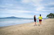 Two women walking on the beach. Rangitoto Island in the background; Milford Beach. Auckland.