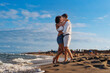 Young romantic couple - embracing lovingly on a sandy beach, enjoying a joyful moment at sunset by the sea - affectionate, warm.
