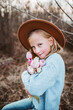 Portrait of a beautiful girl with a hat, holding bouquet of pink tulips. Spring moment, childhood in nature.