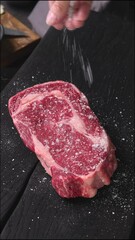 Canvas Print - Chef sprinkles salt on fresh raw beef steak in kitchen, food close-up