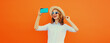 © rohappy - Portrait of happy smiling young woman taking selfie with smartphone wearing straw hat on orange
