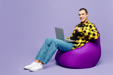 Sticker - Full body young IT middle eastern man wear yellow shirt casual clothes sit in bag chair hold use work point finger on laptop pc computer isolated on plain pastel purple background. Lifestyle concept.