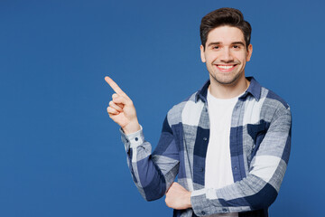 Canvas Print - Young smiling happy Caucasian man he wear shirt white t-shirt casual clothes point index finger aside on area mock up isolated on plain blue cyan color background studio portrait. Lifestyle concept.