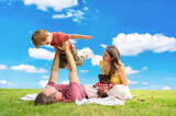 Fototapeta Niebo - happy family spending time on summer day. Father lifted son into the air while picnicking in the park on a summer day.