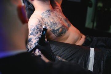 Wall Mural - Male tattoo artist holding a tattoo gun, showing a process of making tattoos on a male tattooed model's arm