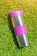 The stainless thermal flask on the green grass background with sunlight. The container for cold or hot beverages for outdoor activity. Selective focus.