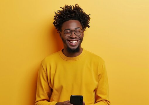 Joyful Young Man with Glasses Laughing Holding Smartphone Yellow Background