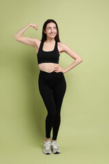 Wall Mural - Happy young woman with slim body showing her muscles on green background