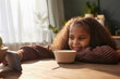Portrait of smiling Black girl using smartphone at kitchen table in morning scene lit by cozy sunlight copy space