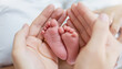 Mother and father hands holding newborn baby feet. Closeup hands of asian parents hold baby feet over white bed. Healthcare love lifestyle happy caucsian family mother’s day together concept
