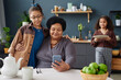 Portrait of loving African American grandmother embracing young girl and looking at smartphone screen in kitchen