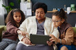 Front view portrait of Black senior woman using digital tablet at home with two children helping