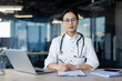 © Liubomir - A focused and thoughtful Asian female doctor with glasses sits at her office desk, equipped with a laptop and medical implements, contemplating her next steps in patient care.