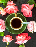 Fototapeta Krajobraz - Coffee time concept; Green cup of coffee and pink roses on a black background; top view