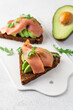 Sandwich with avocado, salmon and grain bread close-up view on white background