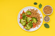 Healthy food broccoli, carrots and chickpeas on plate top view on yellow background with copy space