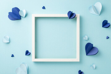 A creative flat lay with paper hearts and an empty frame arranged on a soft blue backdrop, ideal for a variety of design and craft projects