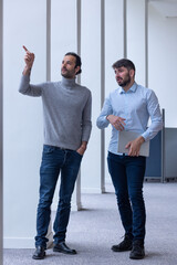 Poster - deux jeune hommes d'affaire ou employés de bureau discutent debout dans les locaux de leur entreprise. l'un d'eux porte un ordinateur portable