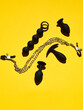 Black sex toys dildo, anal plugs and clamps over yellow paper background