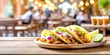 Tacos mit Füllung, im Hintergrund ein Restaurant mit Gästen