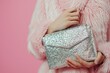 © LimeSky - Woman displaying shiny silver clutch purse on pink backdrop close up of hand