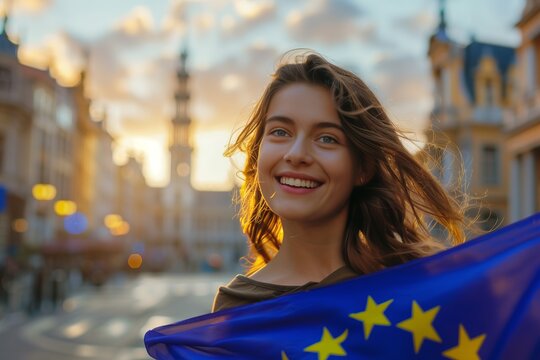 Young smiling woman holding a european union flag in the middle of a square in belgium at sunset. Concept european parliament elections and freedom