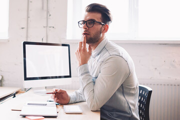 Poster - Caucasian serious male it developer pondering on false on website while sitting at desktop with computer with mock up screen for your internet advertising, concept of technology and communication