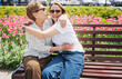 Happy smiling young daughter with senior mother sitting on park bench and hugging, mother day concept