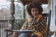 Stunning high resolution photo of a young multi-ethnic woman with attractive almond-shaped eyes wrapped in plaid on a rocking chair on a loggia with a tablet. Business