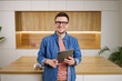 Confident professional in a denim shirt holding a tablet, standing in a modern office with stylish wooden decor.