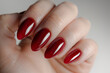 A hand holding a red manicure with a nail polish that has a shiny, glossy finish