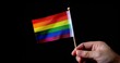 Close up of hand holding small rainbow flag isolated on a black background, representing pride Generative AI